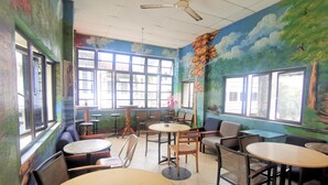 Comedor con varias mesas y sillas, ventanas amplias y un ventilador de techo.