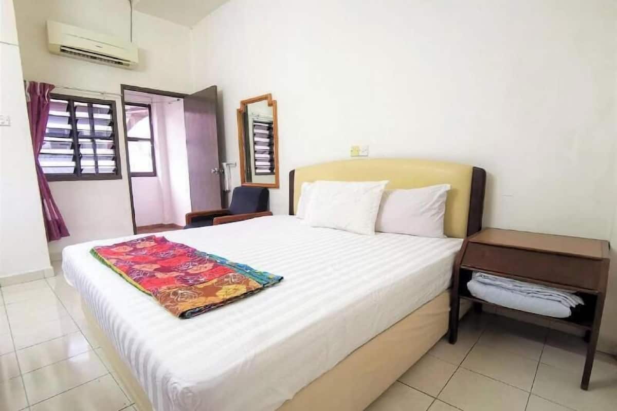 A hotel room with a bed, a nightstand, a chair, an air conditioning unit, and a window with curtains.