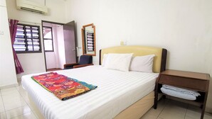 Una habitación de hotel con cama, mesita de noche, una silla, ventana con cortinas y aire acondicionado.