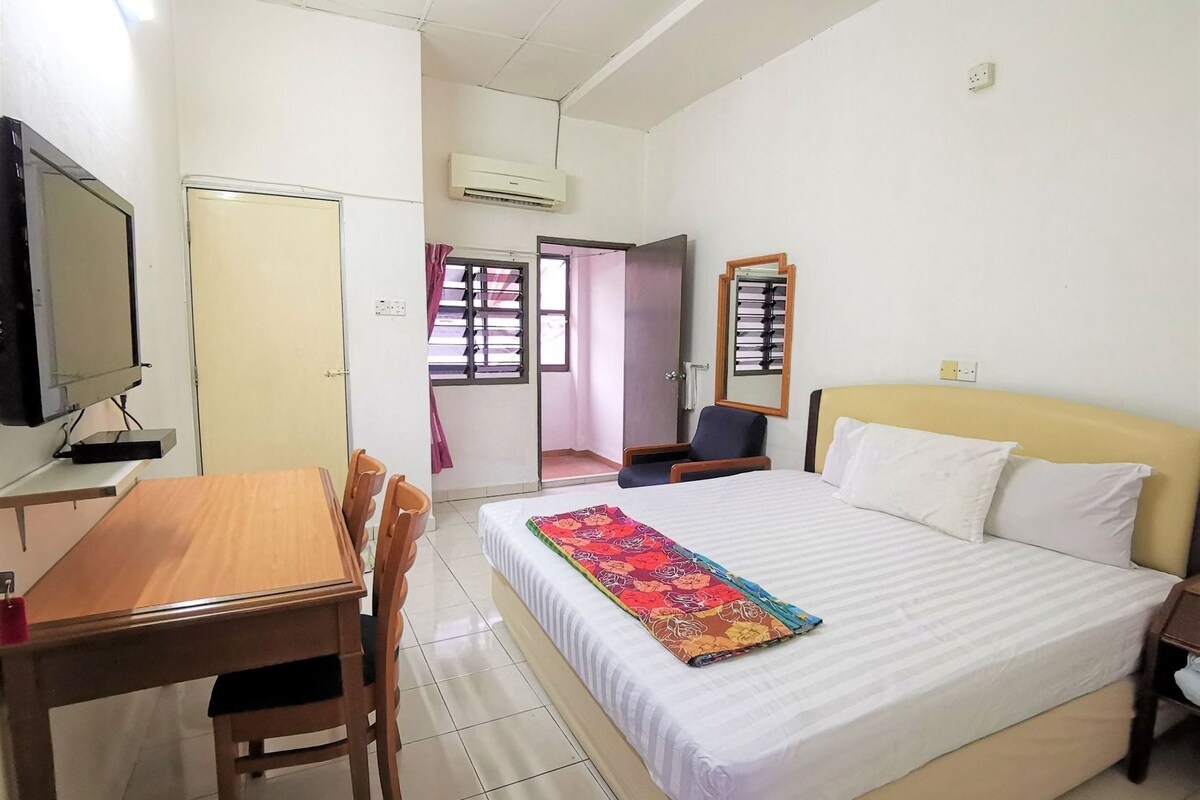 A hotel room with a bed, a desk with chairs, a television, and an air conditioning unit.