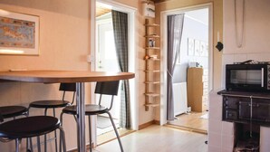 Una cocina compacta con una mesa de madera, taburetes de bar, un microondas y un refrigerador pequeño.
