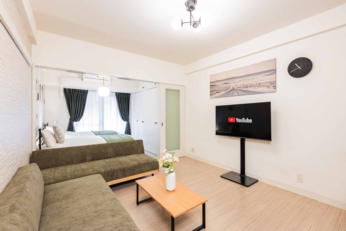 Una sala de estar moderna con un sofá, una mesa de centro con un florero, un televisor de pantalla plana y un cuadro en la pared.