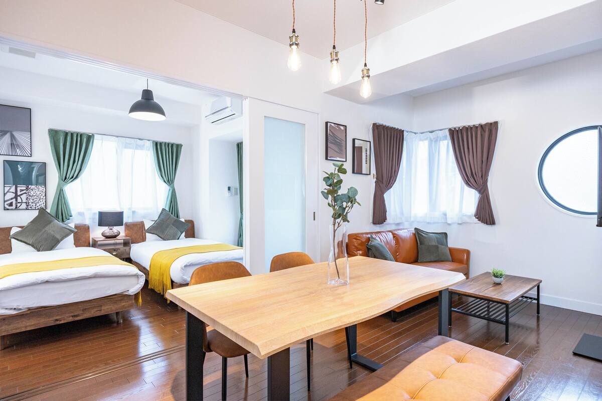 Una habitación de hotel moderna con una mesa de comedor de madera, dos camas, un sofá y una mesita auxiliar.