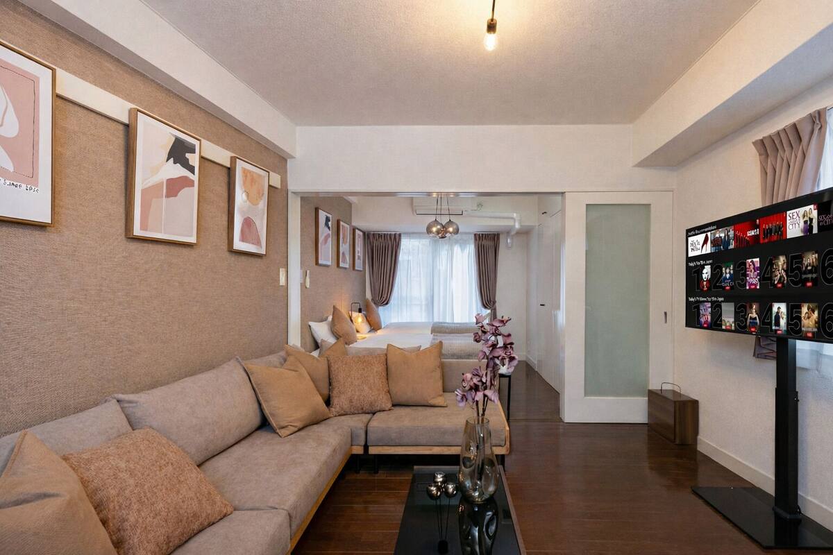 Una sala de estar moderna con un sofá seccional, una mesa de centro y un televisor montado en la pared que muestra carteles de películas.