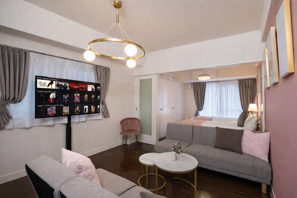 Una sala moderna con una televisión de pantalla plana mostrando recomendaciones de Netflix, un sofá, una mesa de centro y una pequeña silla rosa.