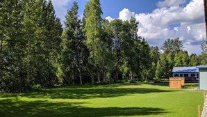 A grassy field with a wooden fence, a shed, and a building with a blue roof. - Talkeetna Inn (Talkeetna)