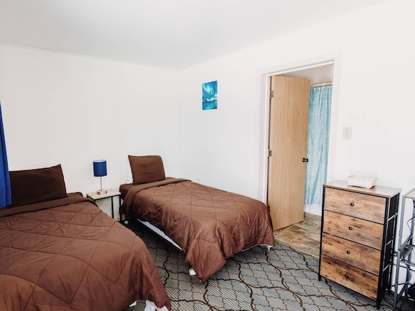 Ein Hotelzimmer mit zwei Betten, einem Nachttisch mit Lampe, einer Holztür und einer Kommode mit Schubladen.