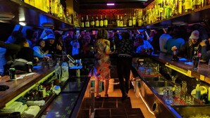 A bar with shelves of bottles, a bartender, and patrons. - Talkeetna Inn (Talkeetna)