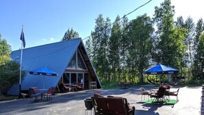 A triangular building with a metal roof, outdoor seating with umbrellas, and a flagpole. - Talkeetna Inn (Talkeetna)