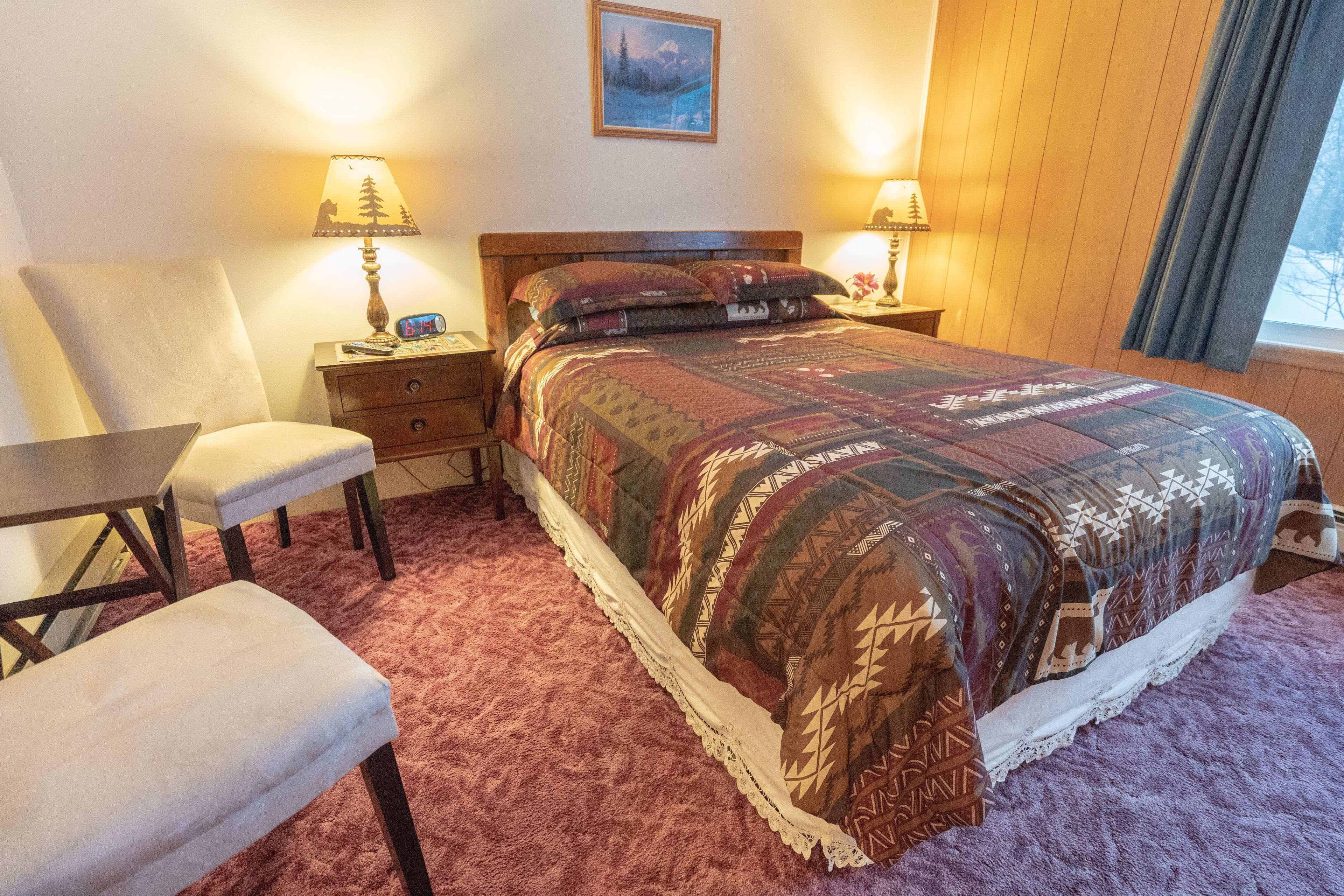 A bedroom with a large bed, two bedside tables with lamps, a chair, and a desk.