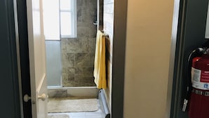 A bathroom with a stone shower, a towel rack with a yellow towel, and a fire extinguisher on the wall. - Best Location (Cody)