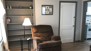 A living room with a brown armchair, a lamp, a bookshelf, and a door. - Best Location (Cody)