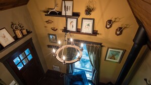 Een gezellige kamer met een houten plafond, een open haard, een blauwe fauteuil en diverse ingelijste foto's aan de wanden.