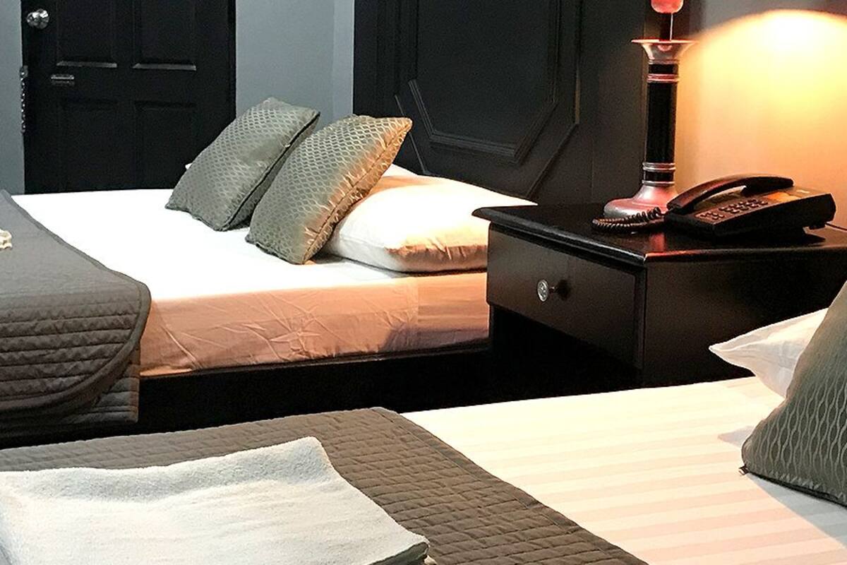 A hotel room with two beds, a bedside table with a lamp, a phone, and a small cabinet.
