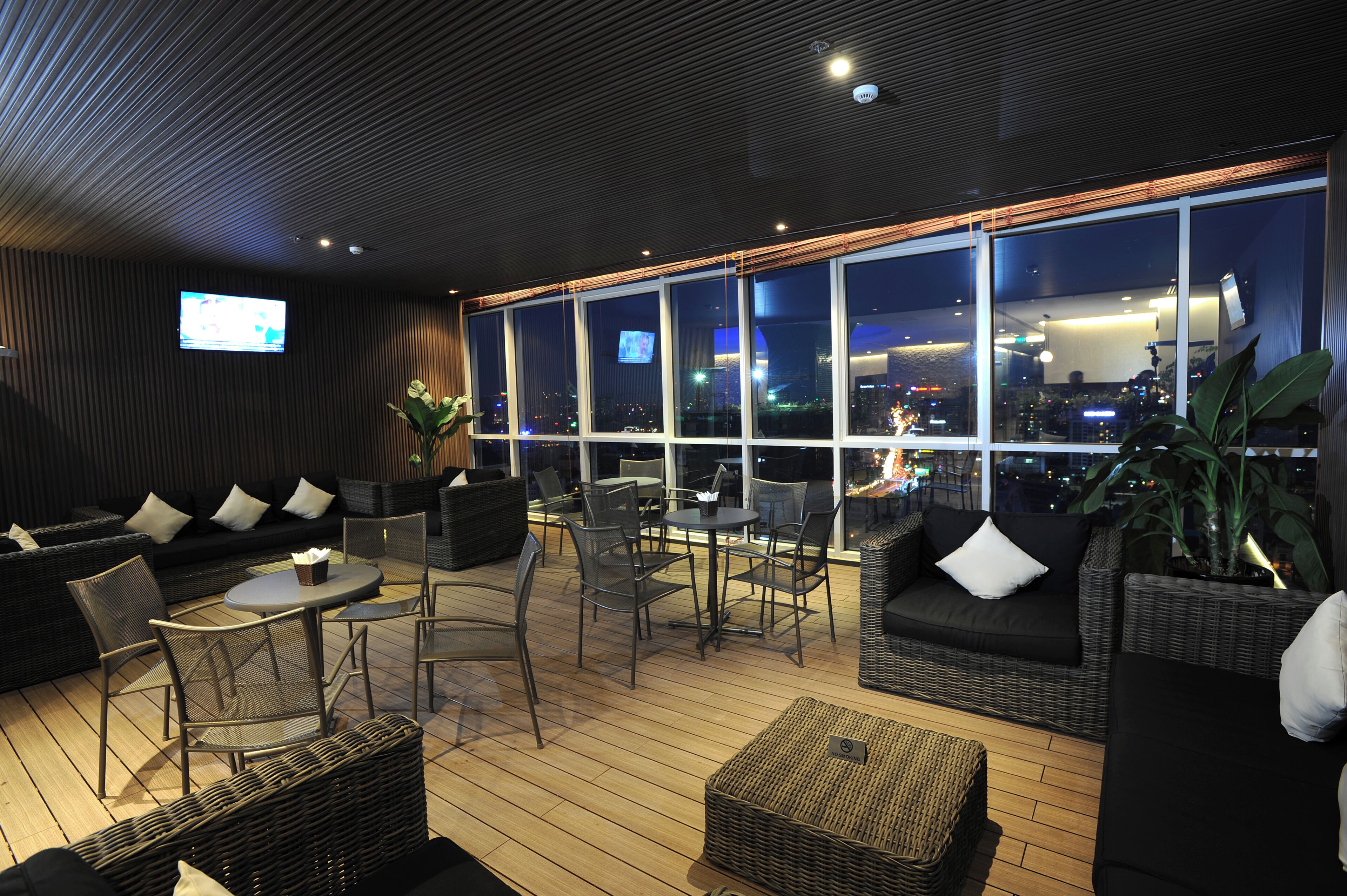 A modern lounge area with a city view, featuring sofas, chairs, a table, and a TV screen.