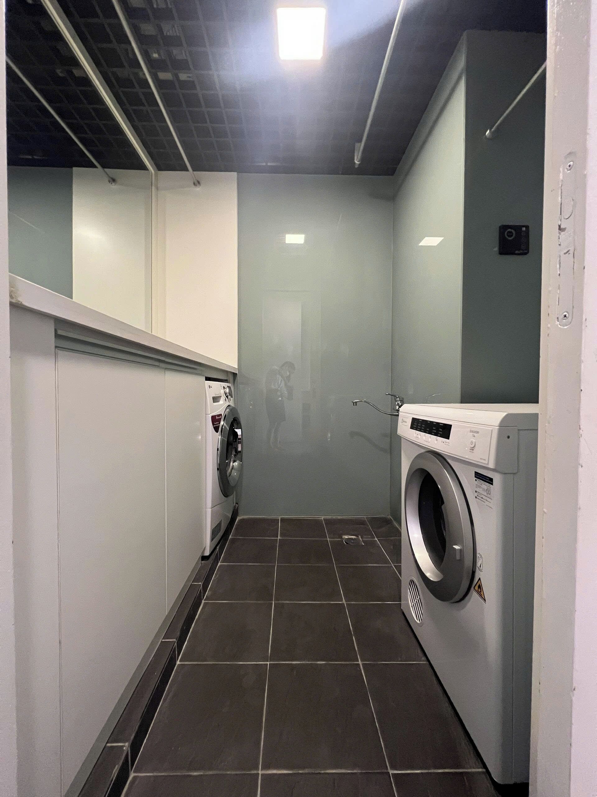 A laundry room with two washing machines, a tiled floor, and a ceiling with a grid pattern.