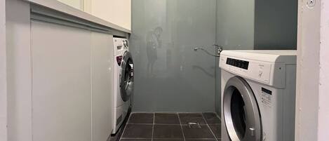 A laundry room with two washing machines, a tiled floor, and a ceiling with a grid pattern.