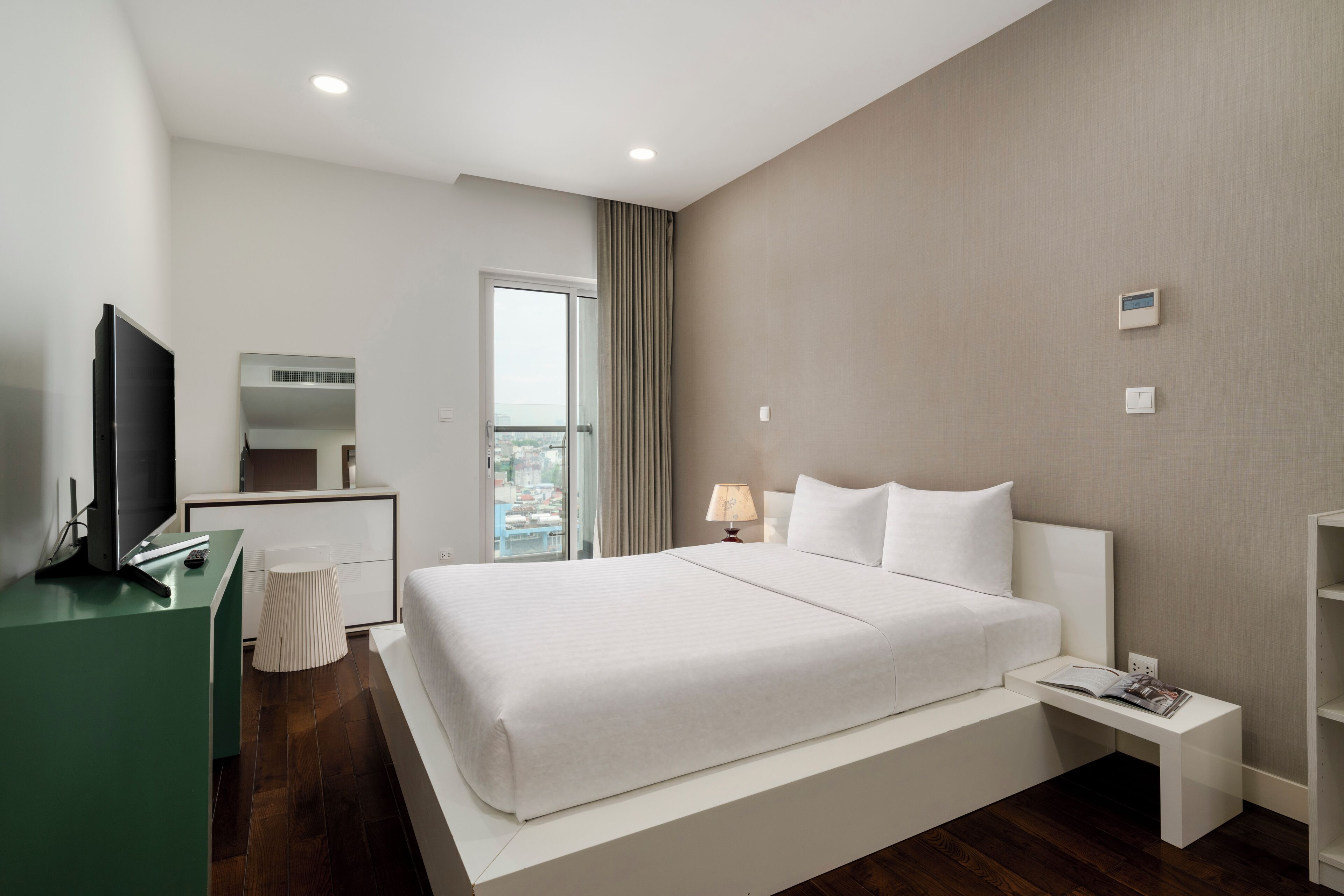 A modern hotel room with a large bed, a desk, a TV, and a view of the city.