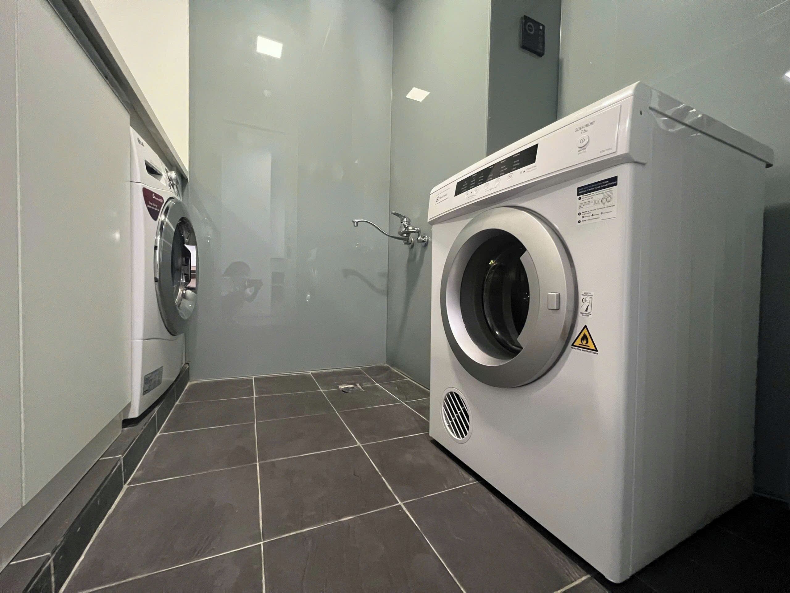 A modern laundry room with a front-loading washing machine and a dryer, tiled floor, and a visible water pipe.
