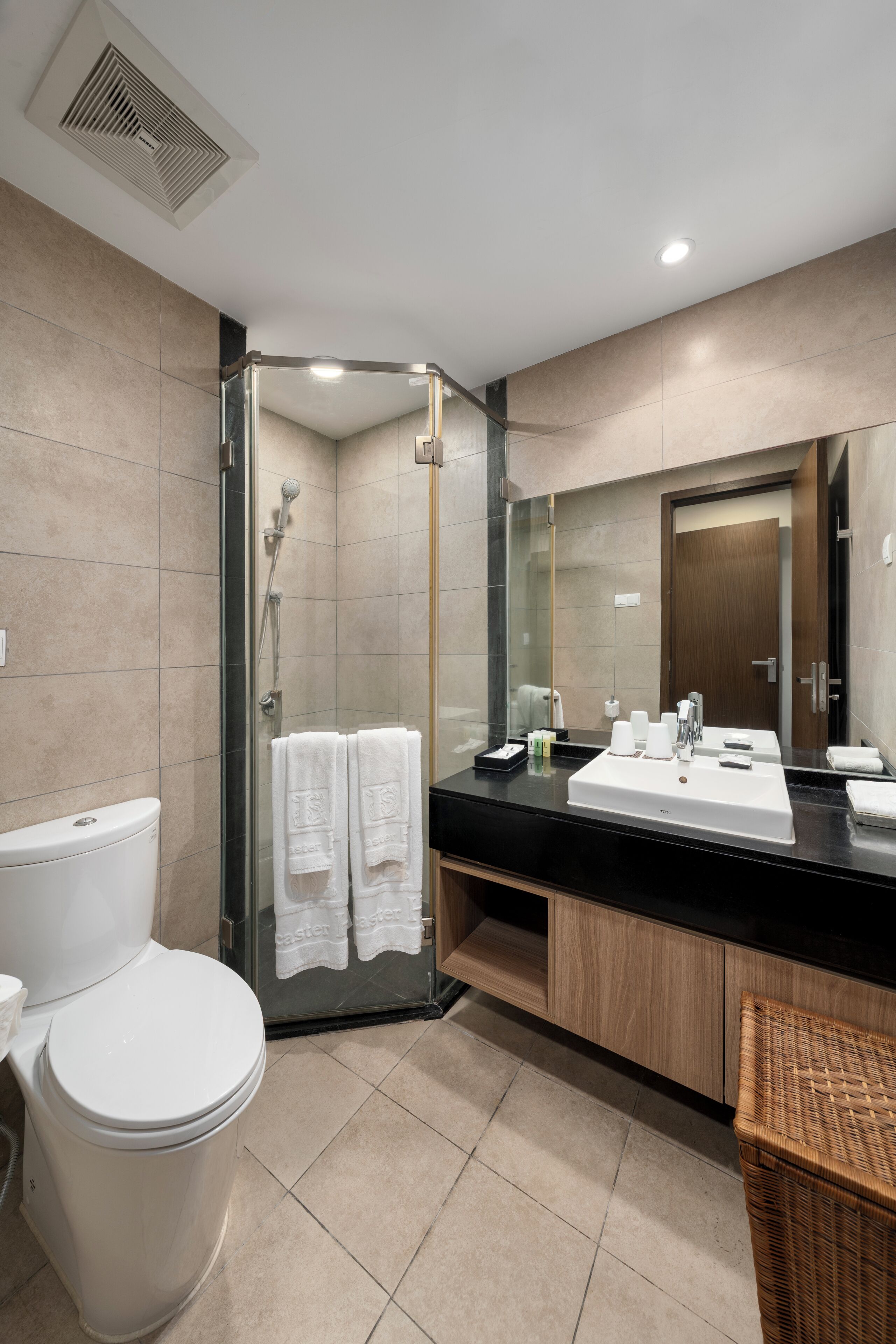 A modern bathroom with a glass-enclosed shower, a white toilet, a sink with a mirror, and a wicker basket.