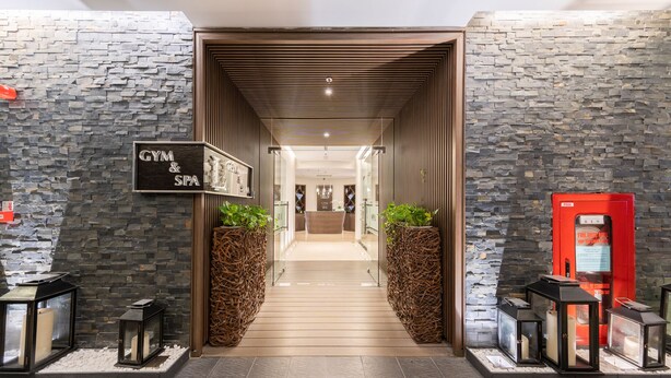 A modern hotel lobby with a stone wall, a sign for a gym and spa, and a red fire extinguisher. - Lancaster Hanoi Service Apartment (Hanoi)
