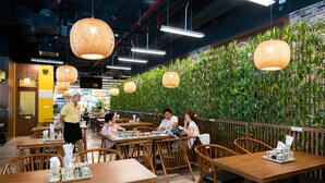 A restaurant with wooden tables and chairs, hanging wicker lamps, and a bamboo wall. - Lancaster Hanoi Service Apartment (Hanoi)