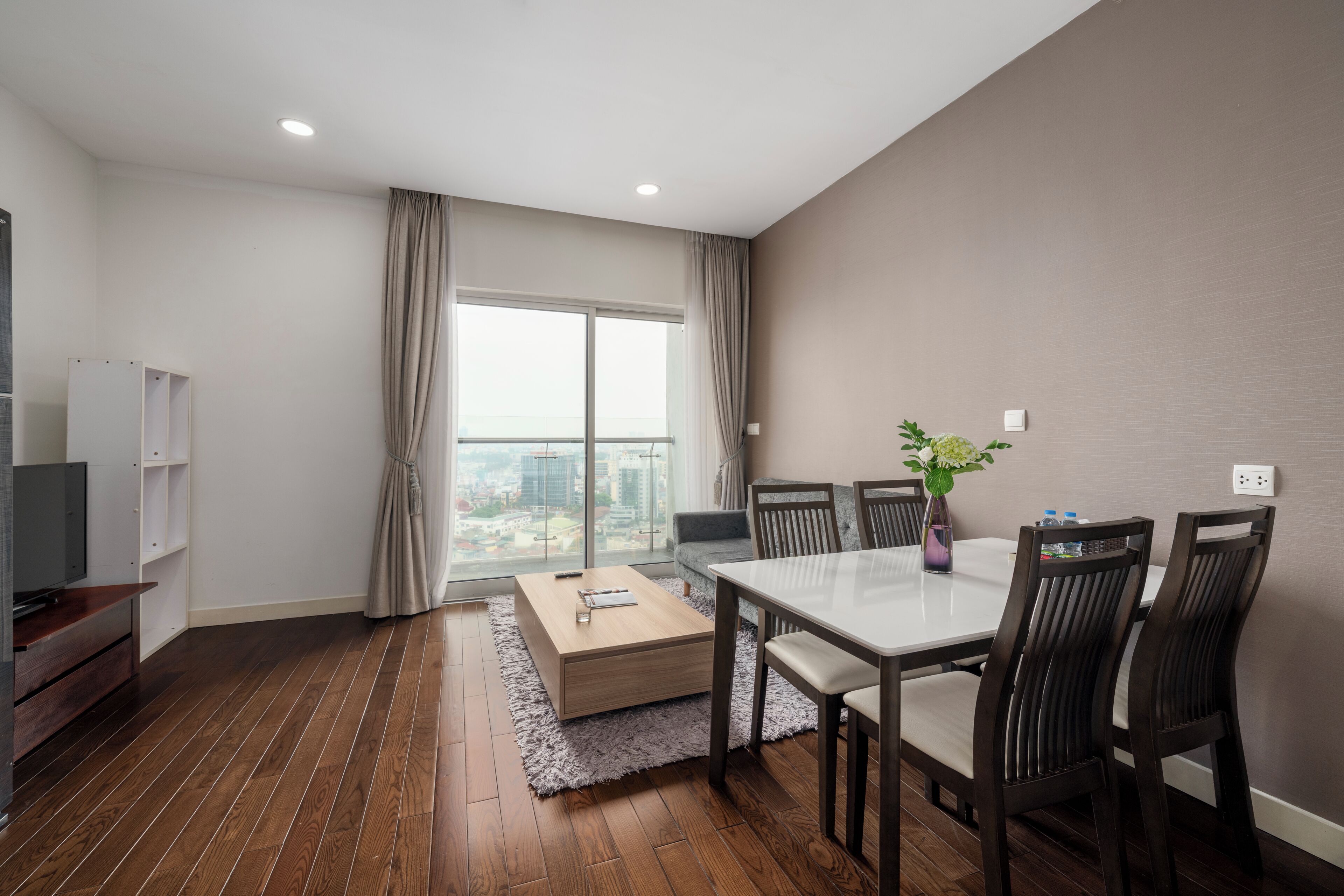 A modern living room with a dining table, chairs, a TV, and a large window with curtains.