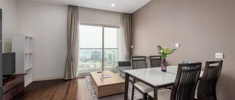 A modern living room with a dining table, chairs, a TV, and a large window with curtains.