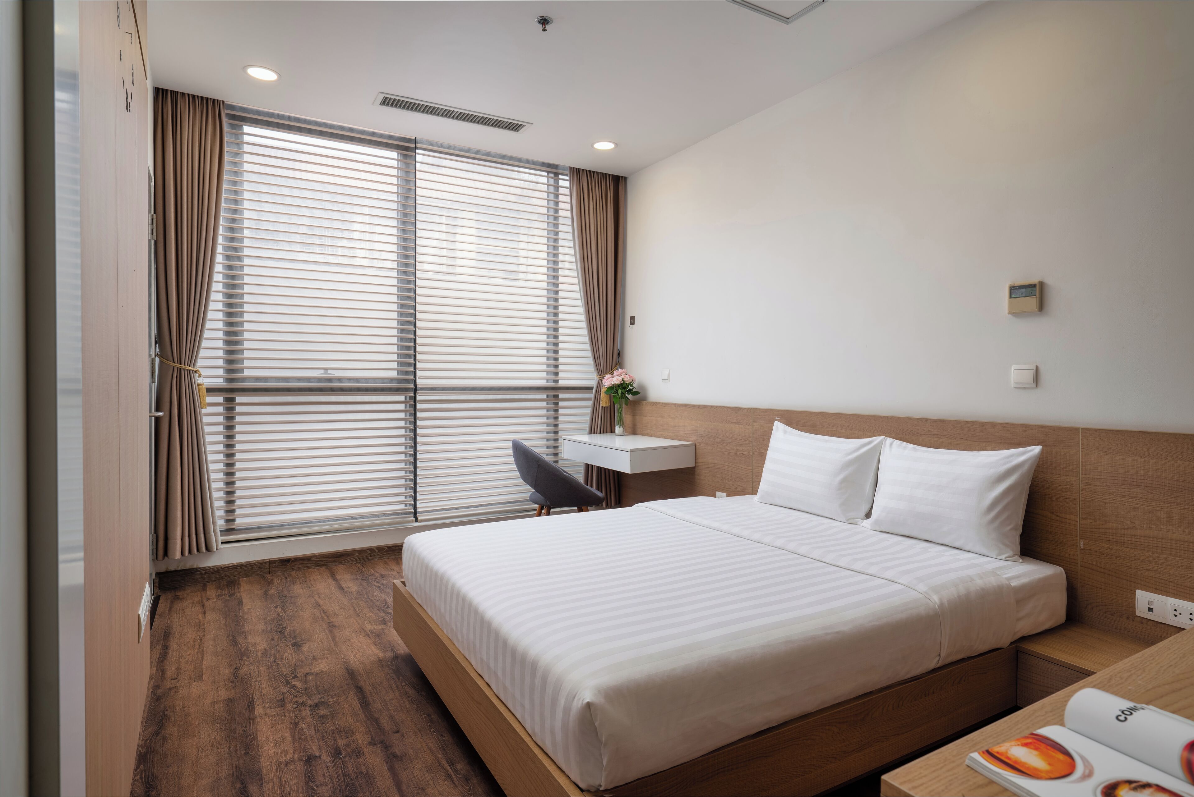 A hotel room with a large bed, a desk, a chair, and a window with blinds.