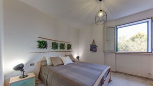 Ein Schlafzimmer mit Bett, Nachttisch, Lampe, Wandpflanzen und einem Fenster mit Blick.