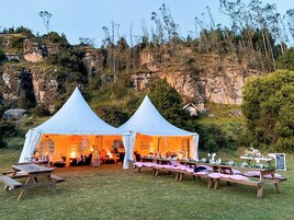 Dos tiendas blancas montadas sobre un campo de césped, con mesas y sillas dispuestas para un evento.