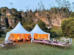 Dos tiendas blancas montadas sobre un campo de césped, con mesas y sillas dispuestas para un evento.