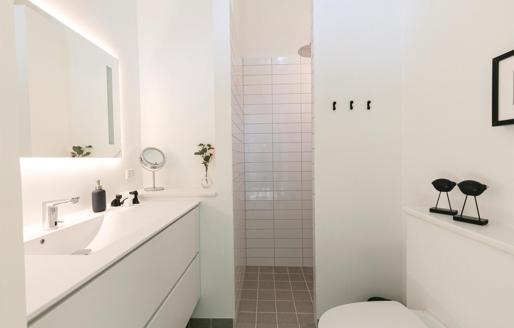 A modern bathroom with a white vanity, a mirror, a small plant, and a shower area.