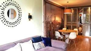 A modern living room with a purple sofa, a round mirror, and a dining area with a table and chairs.