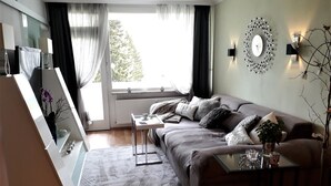 A modern living room with a sofa, a coffee table, a side table, and a large window with curtains.