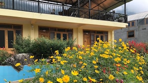 A hotel with a yellow facade, balconies, and a pool surrounded by vibrant yellow and red flowers. - Sau Meo Homestay (Ta Van)