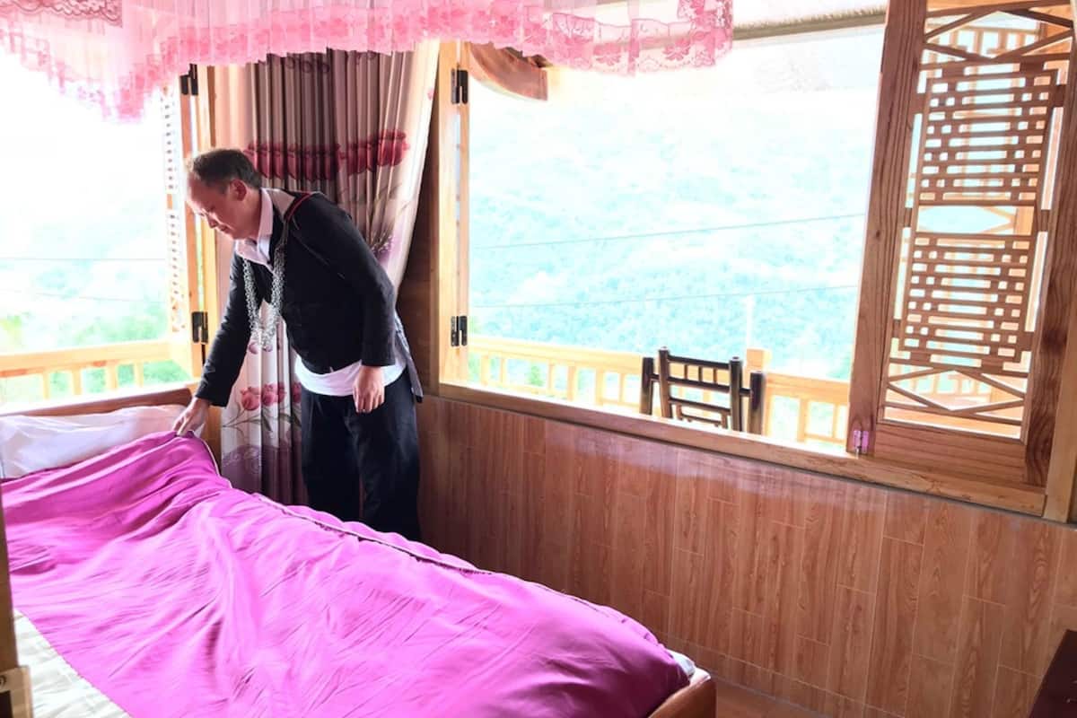 A room with a bed, wooden walls, a window with a view, and a wooden railing outside.