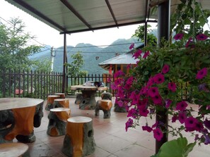 An outdoor seating area with stone stools and tables, surrounded by a metal fence, with a view of mountains in the background. - Sau Meo Homestay (Sa Pa)
