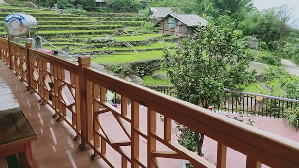 A wooden balcony with a view of terraced rice fields and a small house in the background. - Sau Meo Homestay (Ta Van)