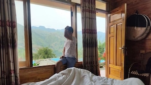 A bedroom with a bed, a window with curtains, and a view of mountains. - Sau Meo Homestay (Ta Van)