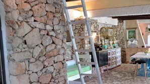 A stone wall with a wooden ladder, a red chair, and a table with a fan in a rustic interior.