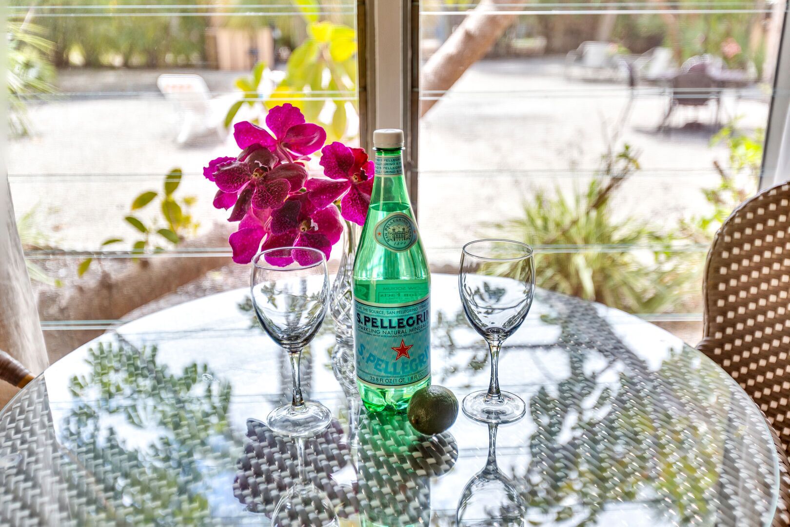 Uma mesa com uma garrafa de água mineral gaseificada S. Pellegrini, dois copos de vinho e um arranjo de flores.