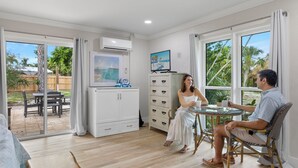 Ein Zimmer mit einer Schiebetür zu einer Terrasse, einem weißen Schrank, einem an der Wand befestigten Fernseher und einem Esstisch mit Stühlen.
