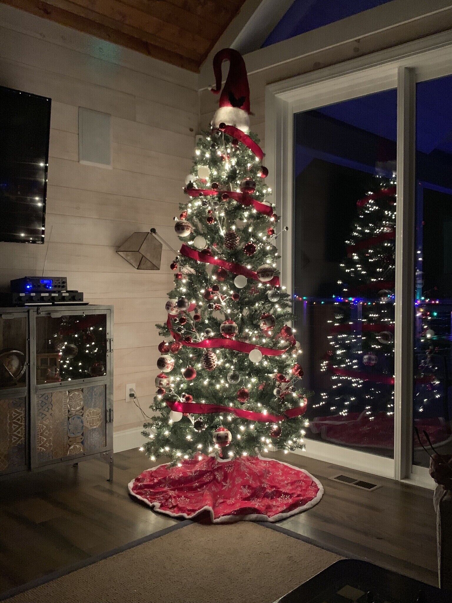 Un sapin de Noël décoré de guirlandes lumineuses et d’ornements, une jupe rouge et un bonnet de Père Noël.