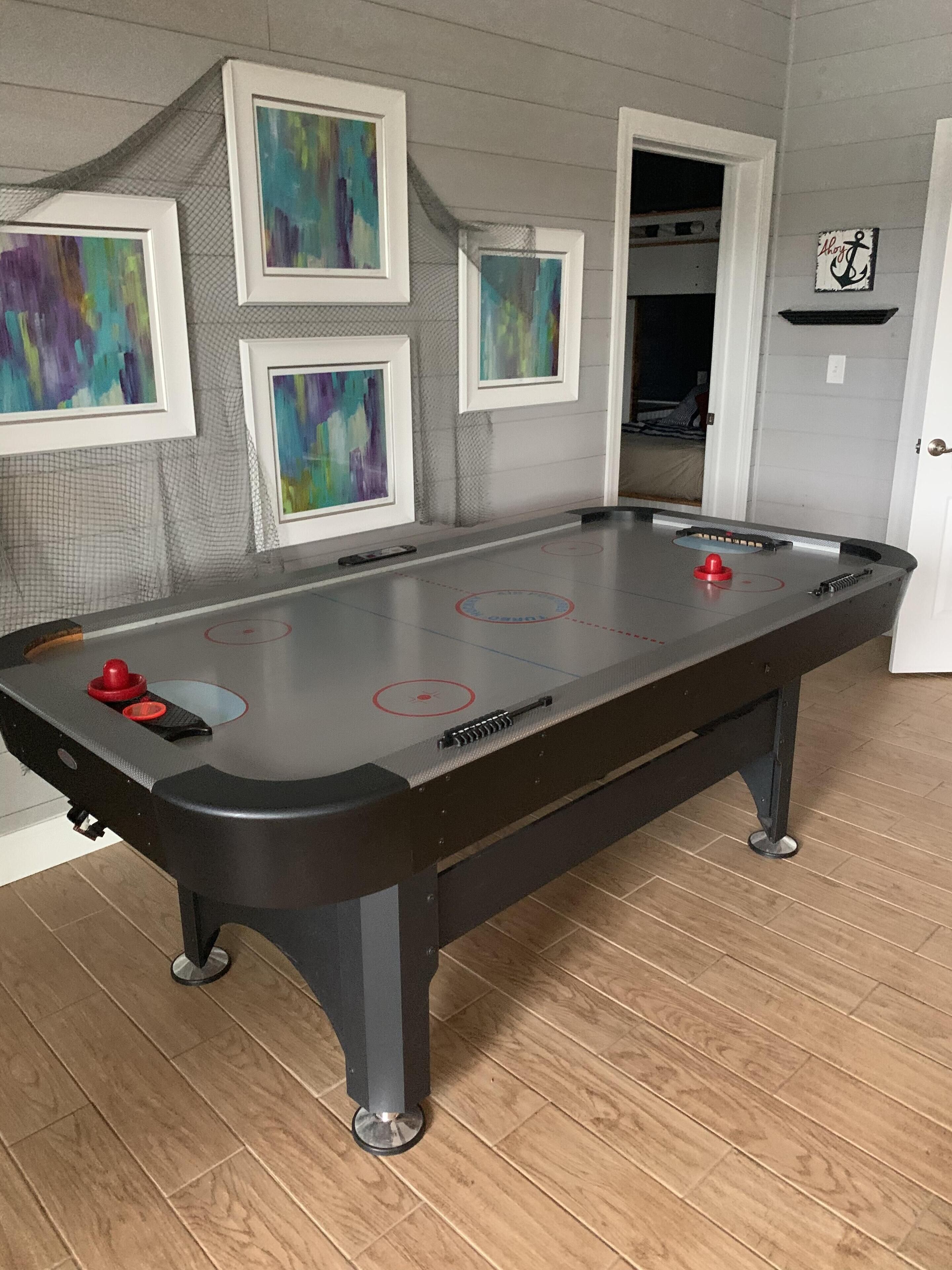 A pool table with a netted wall and framed abstract paintings.