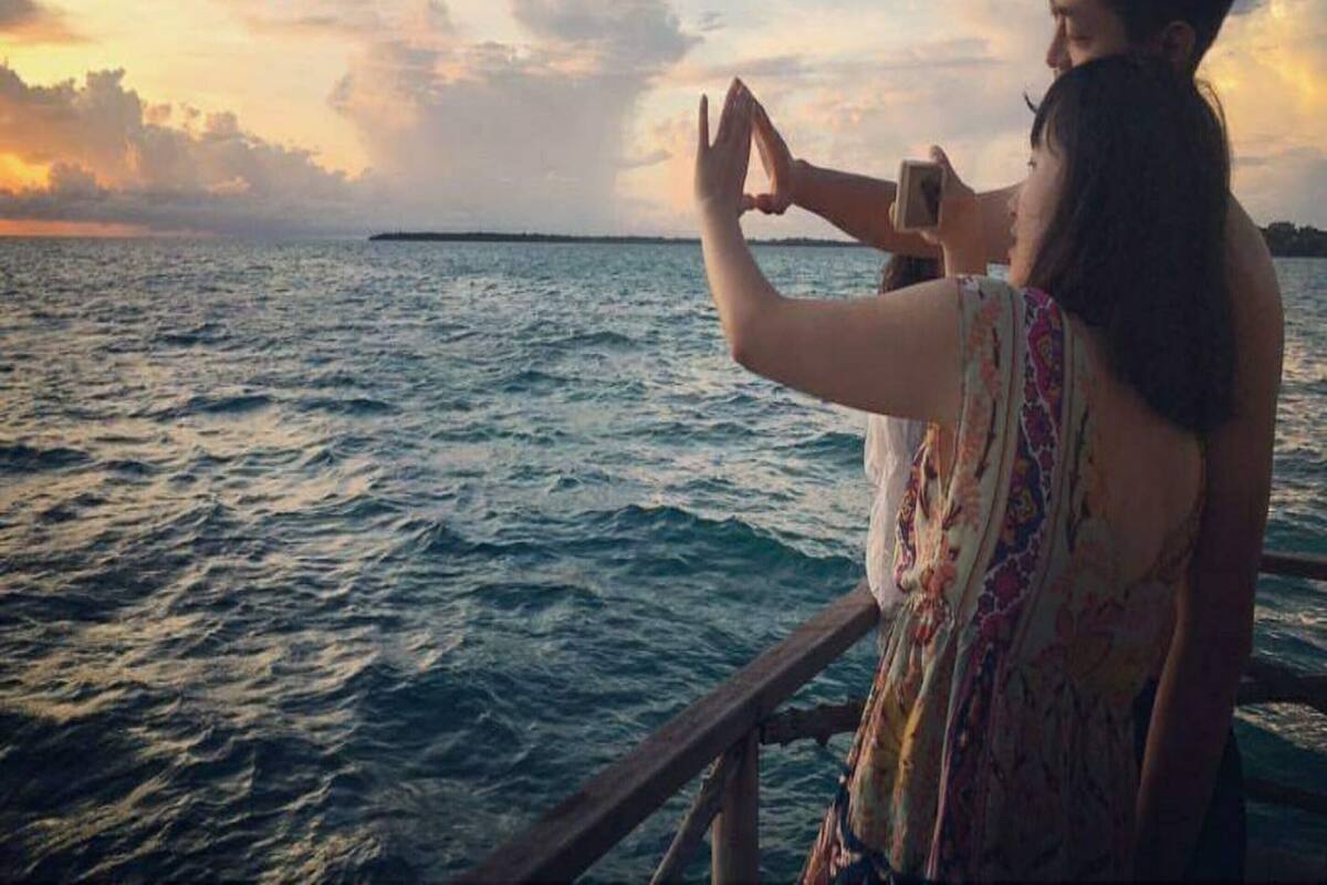 A couple on a boat with a view of the sea and a distant island.