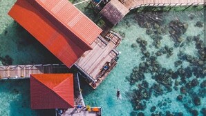 An aerial view of a resort with a large building, a dock with a boat, and clear turquoise waters. - Lato Lato Resort (Semporna)