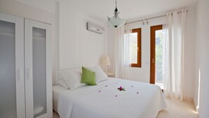 Ein Schlafzimmer mit Bett, Kleiderschrank, Klimaanlage, Lampe und zwei fensterbepflanzten Fenstern.