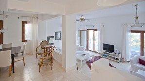 Ein geräumiges Wohnzimmer mit Essbereich, einem weißen Sofa, einem Fernseher und einem Deckenventilator.