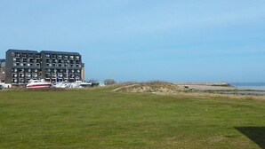 Un edificio moderno a più piani con tetto piatto, situato vicino a una spiaggia con un prato in primo piano.